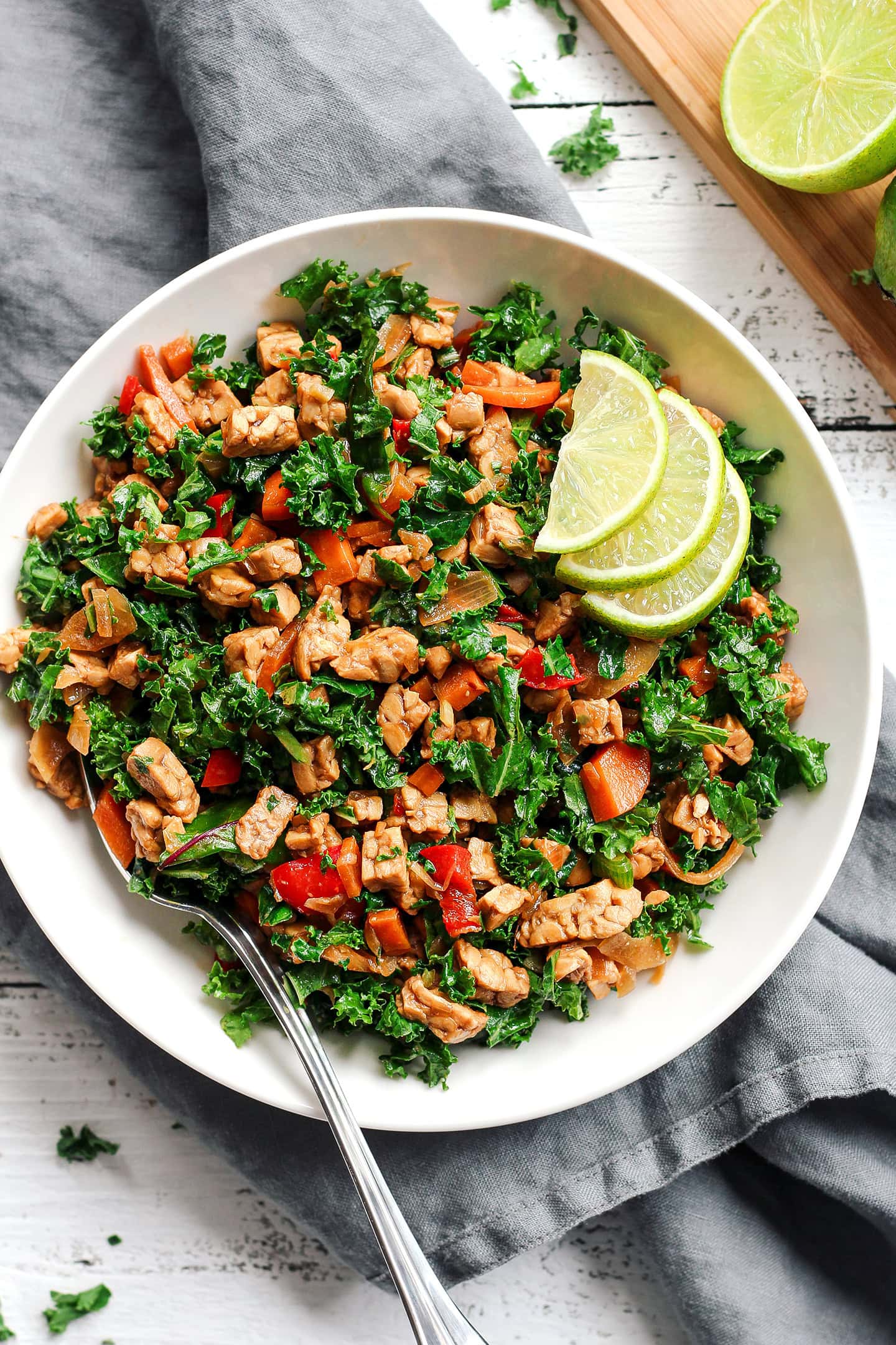 Tempeh salad with kale, bell peppers, carrots, and lime in a white plate.