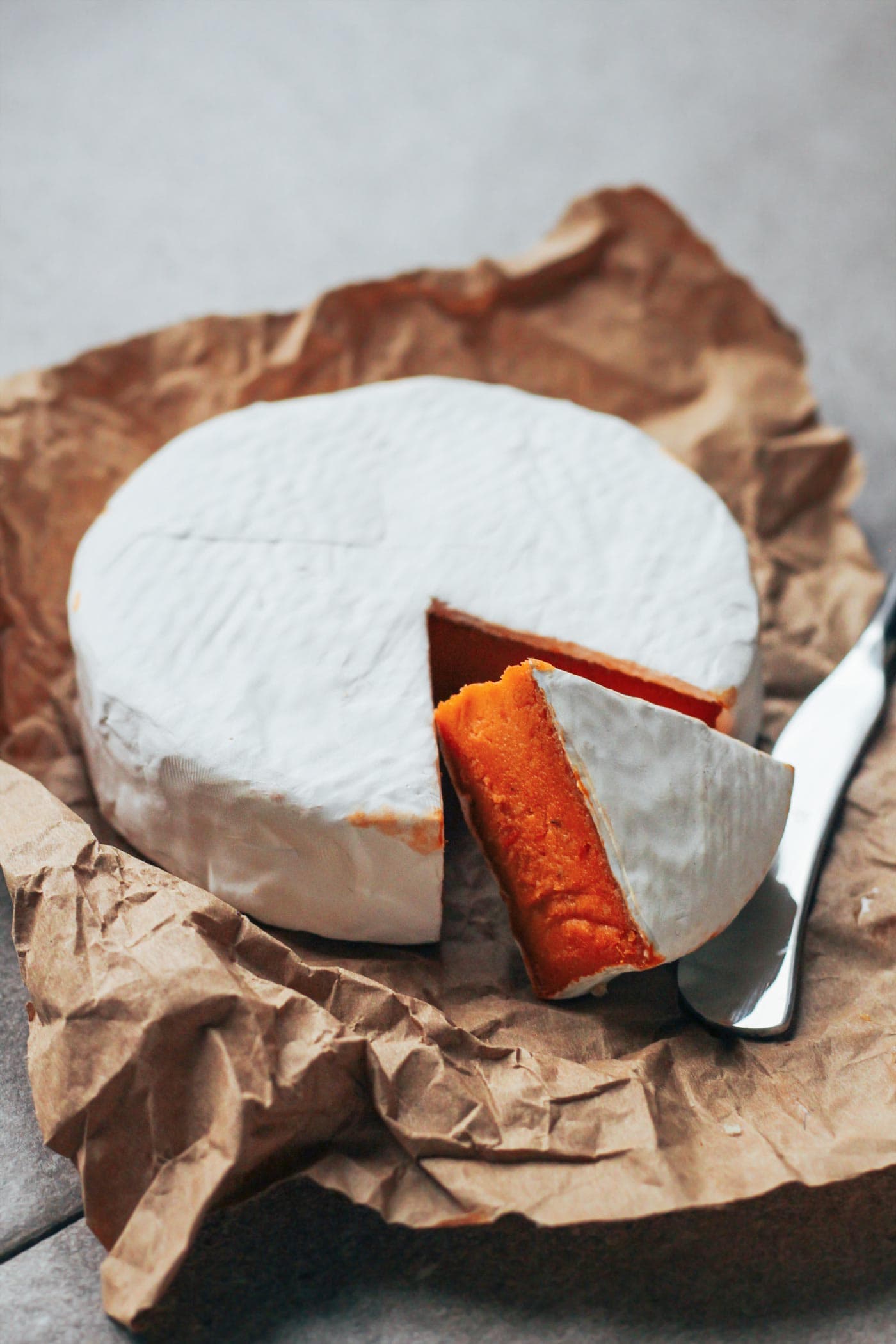 Wheel of vegan sun-dried tomato camembert on a layer of parchment paper.