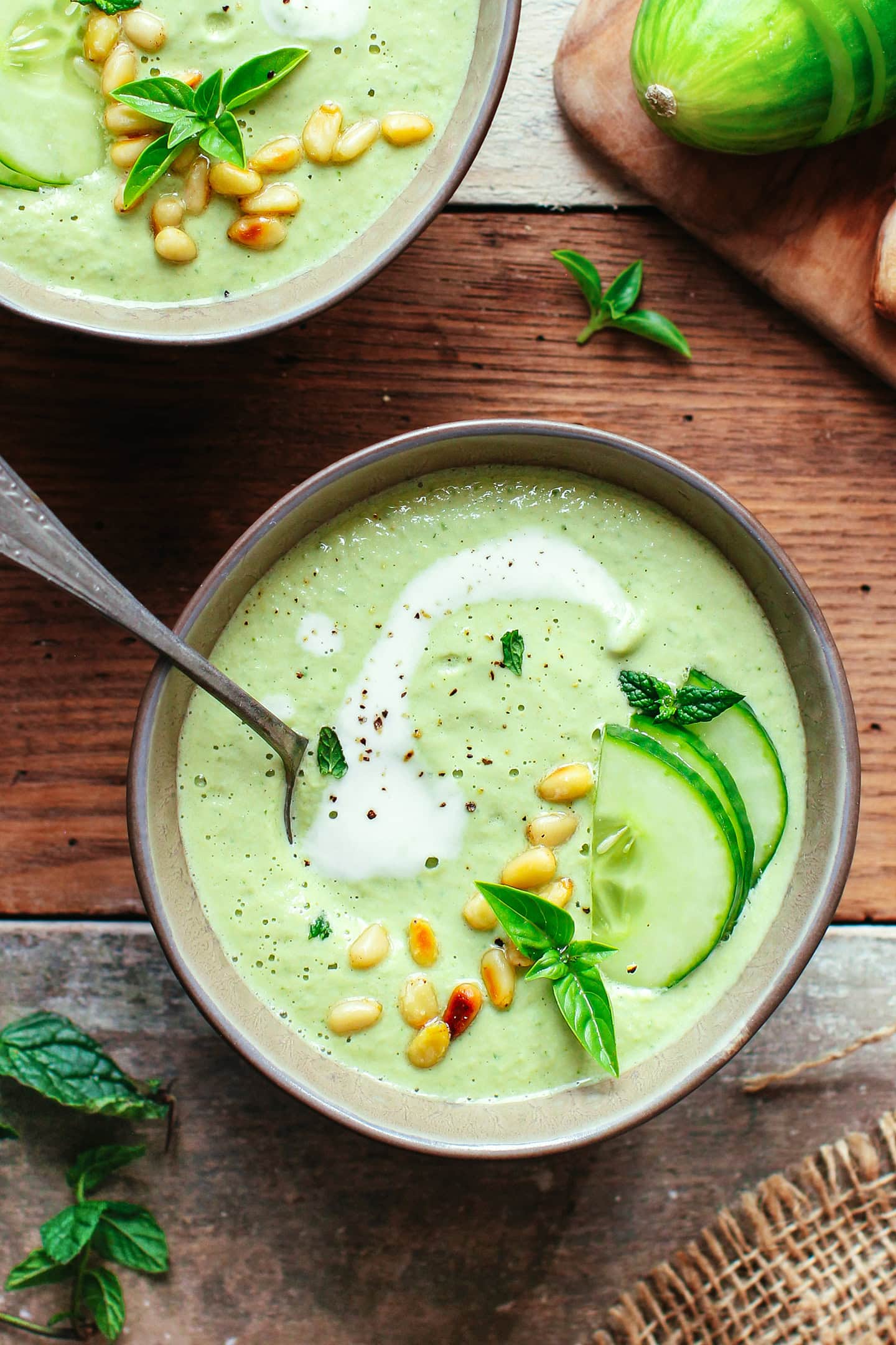 Bowl of cucumber gazpacho with pine nuts, mint, basil, and sliced cucumbers.