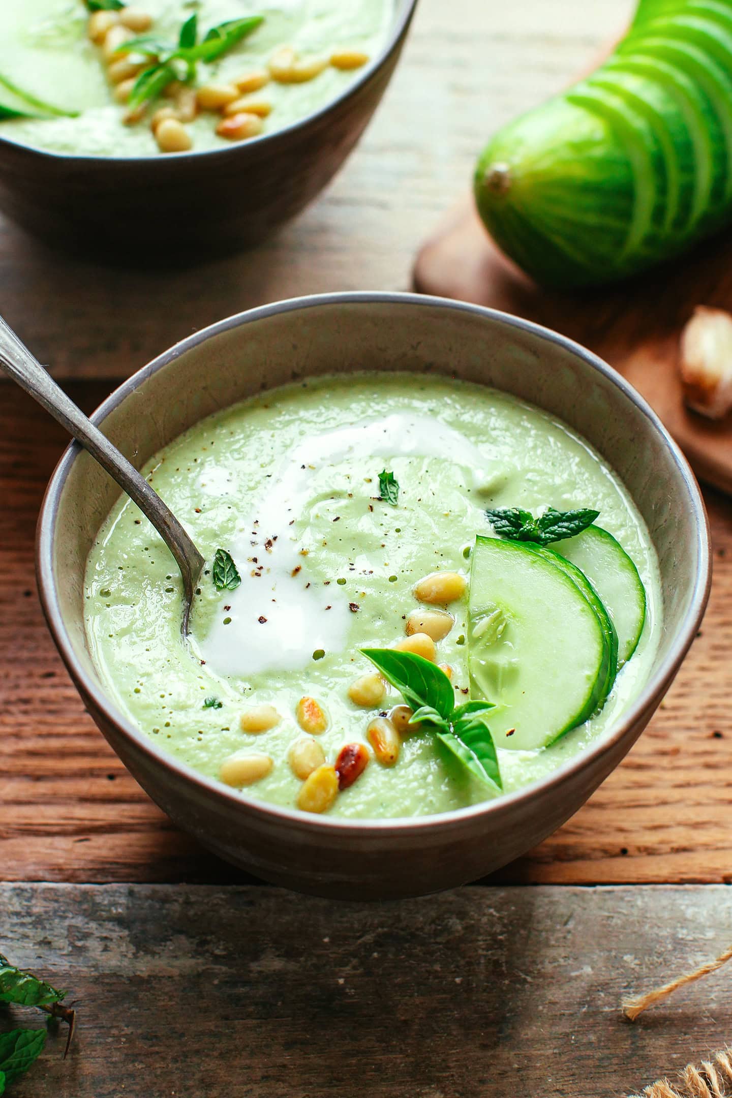 Bowl of cucumber gazpacho with pine nuts, basil leaves, and cucumber slices.