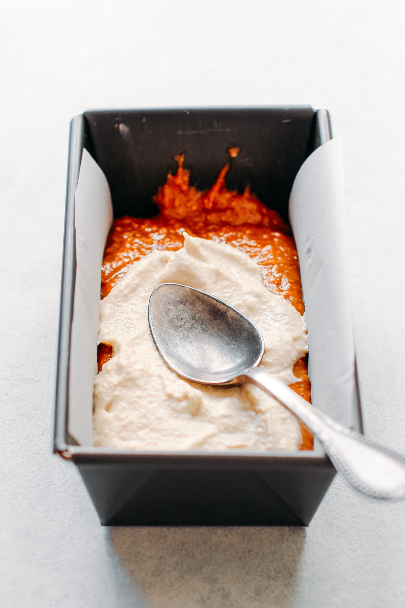 Spreading vanilla cream cheese on top of a banana bread batter.