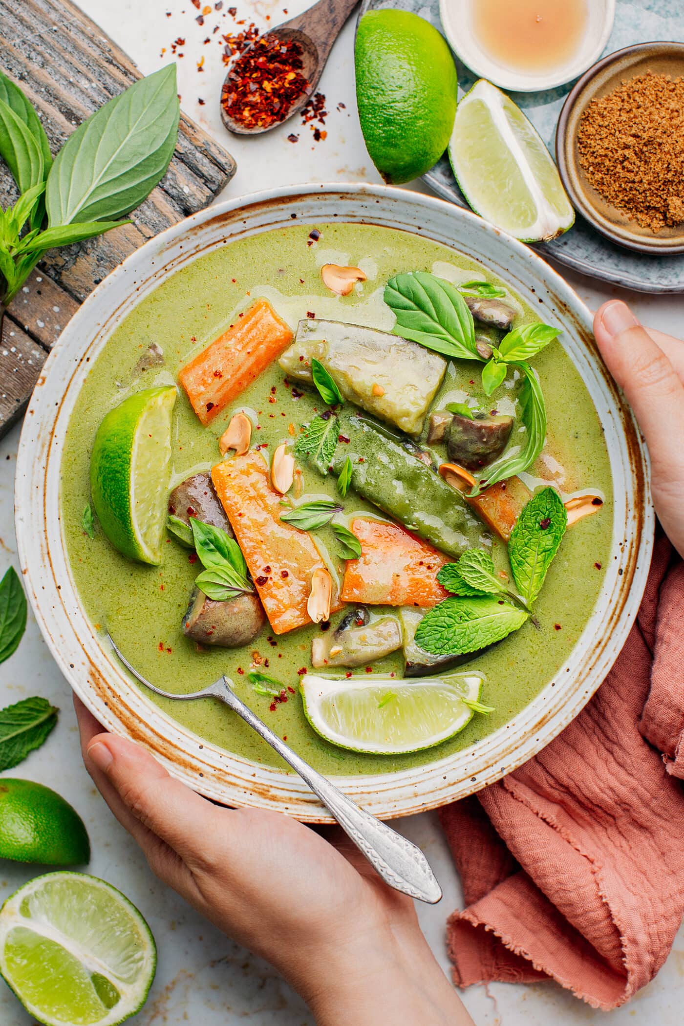 Holding a bowl of green curry topped with fresh herbs.