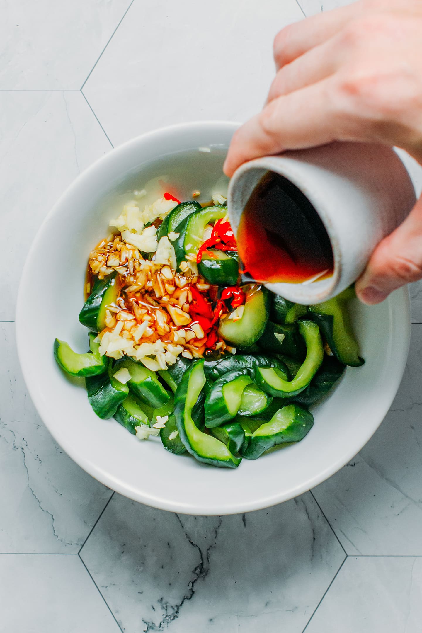 Coating sliced cucumbers with soy sauce, garlic, and chili.