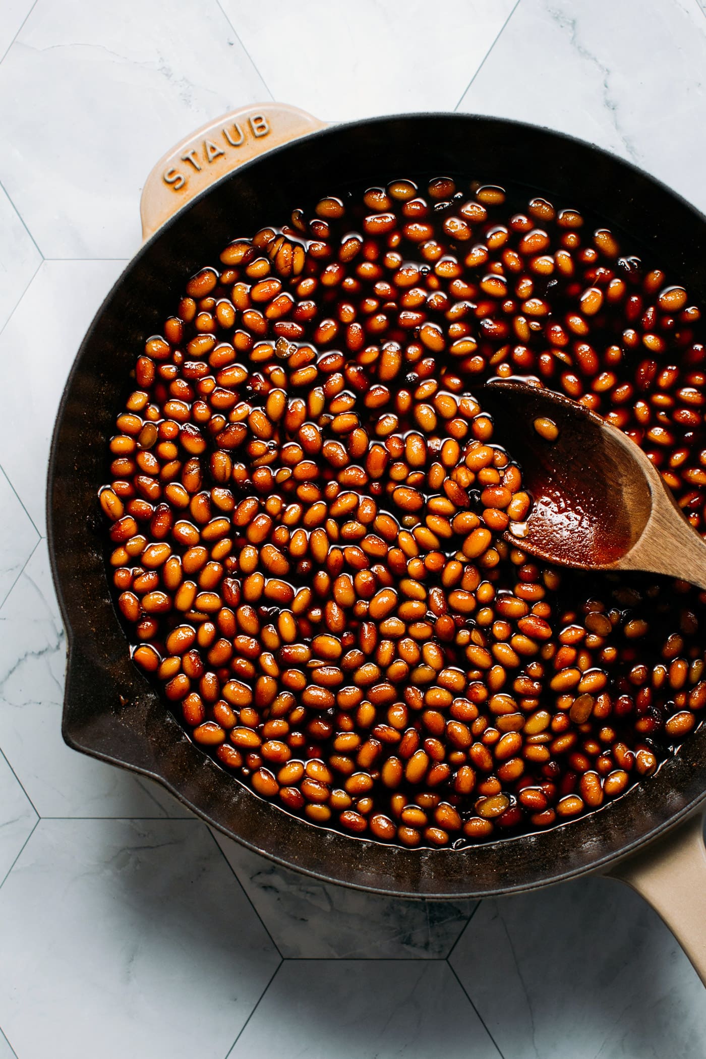 Whole soybeans in a skillet with soy sauce and sugar.