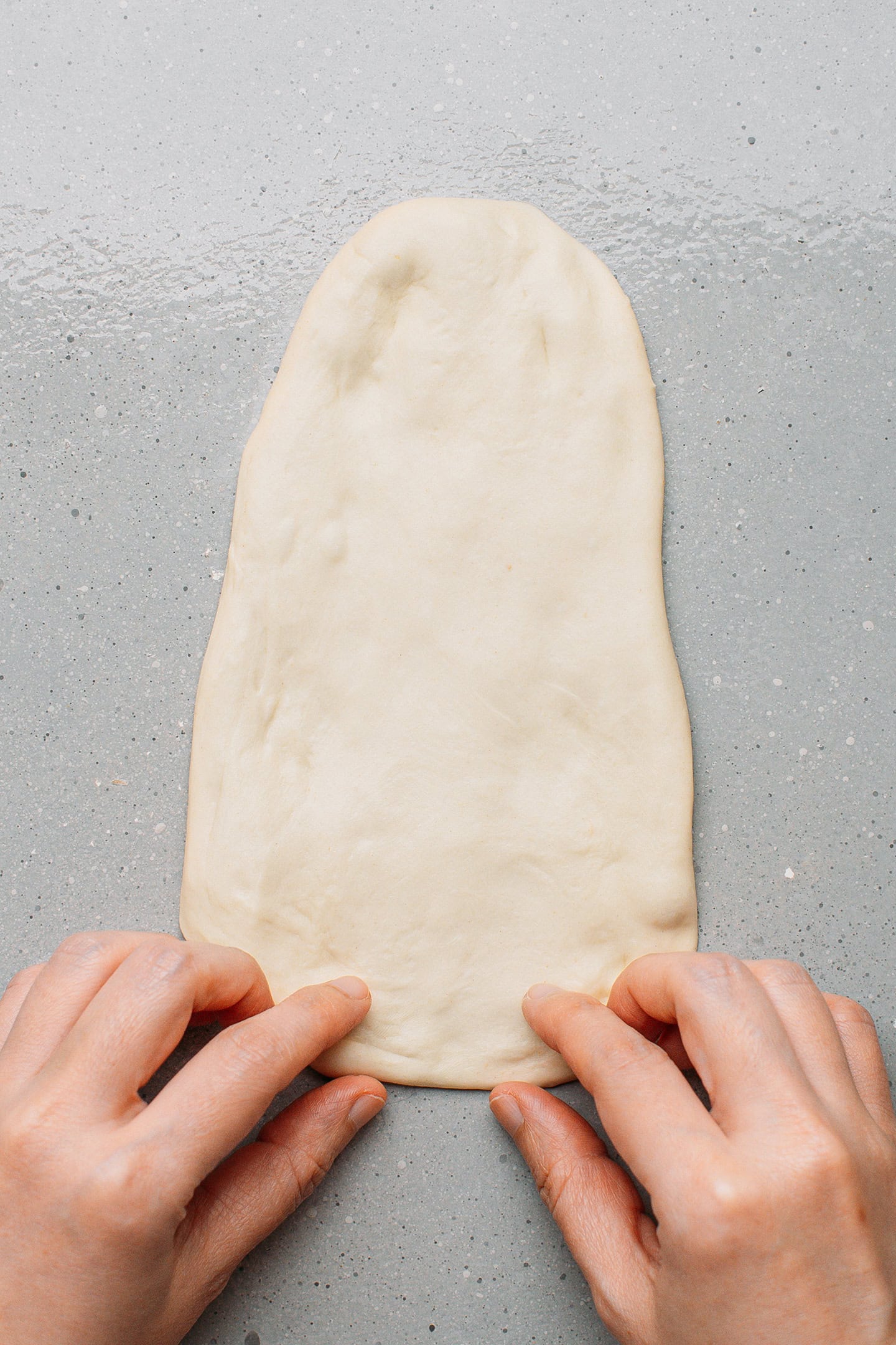 Flattening a bread dough into a long triangle.