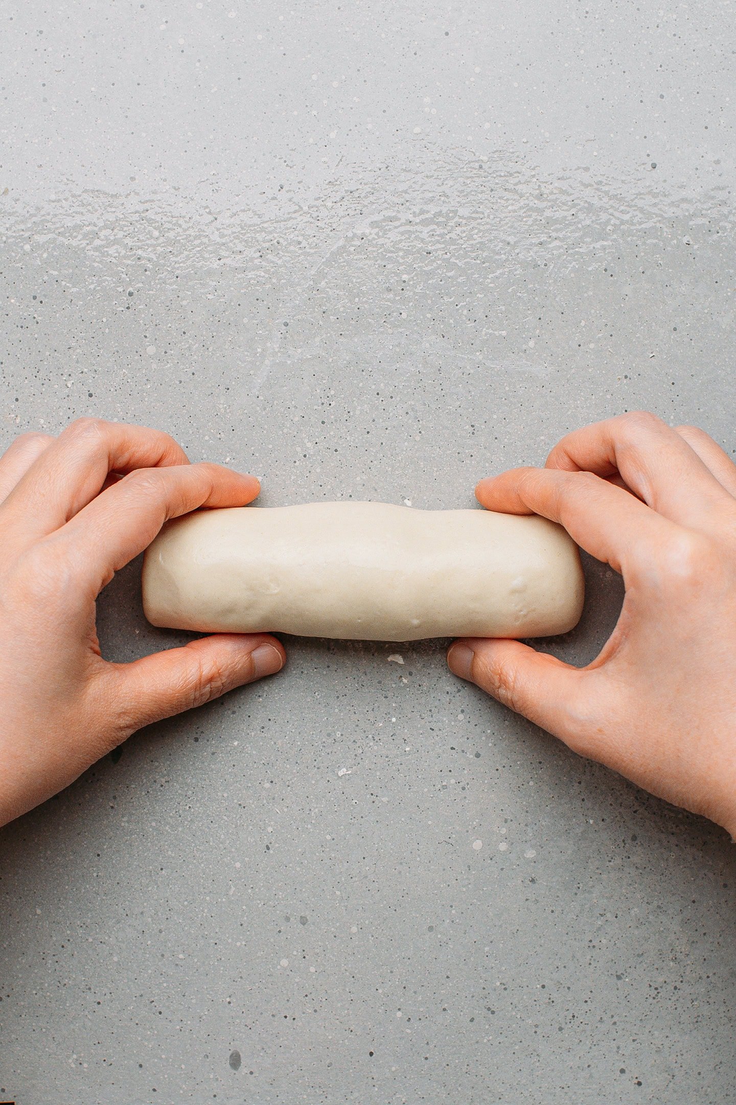 Rolling a ball of dough into a long log.