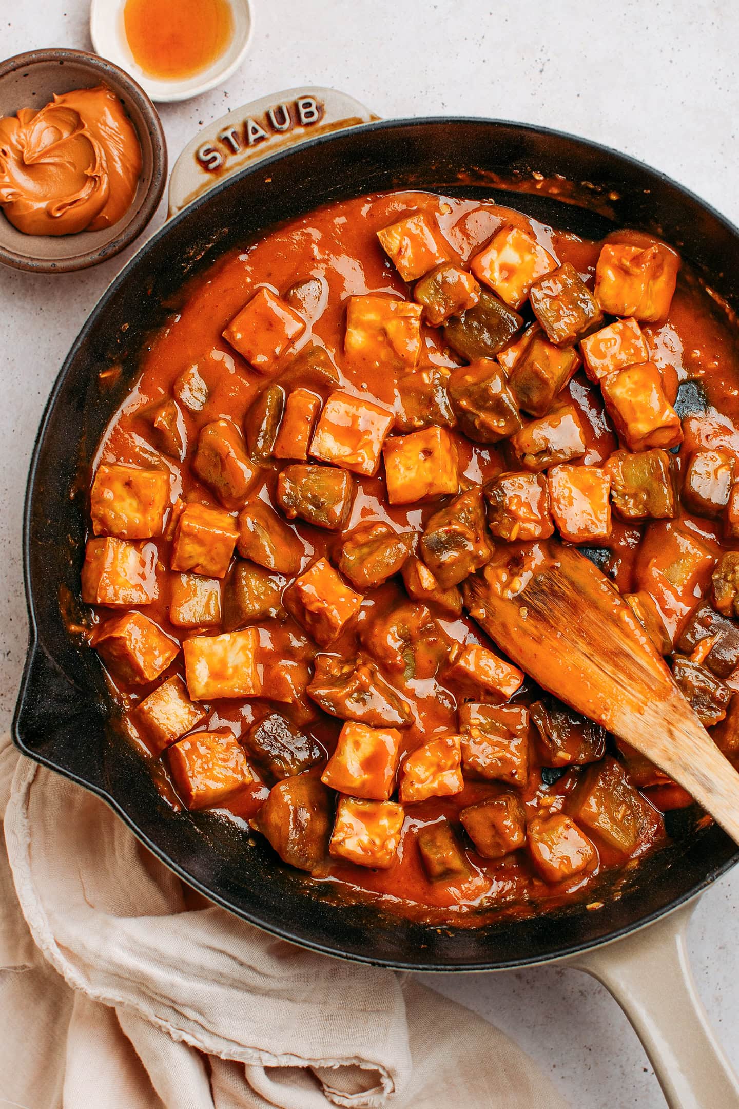 Diced eggplant and tofu tossed with peanut sauce in a skillet.