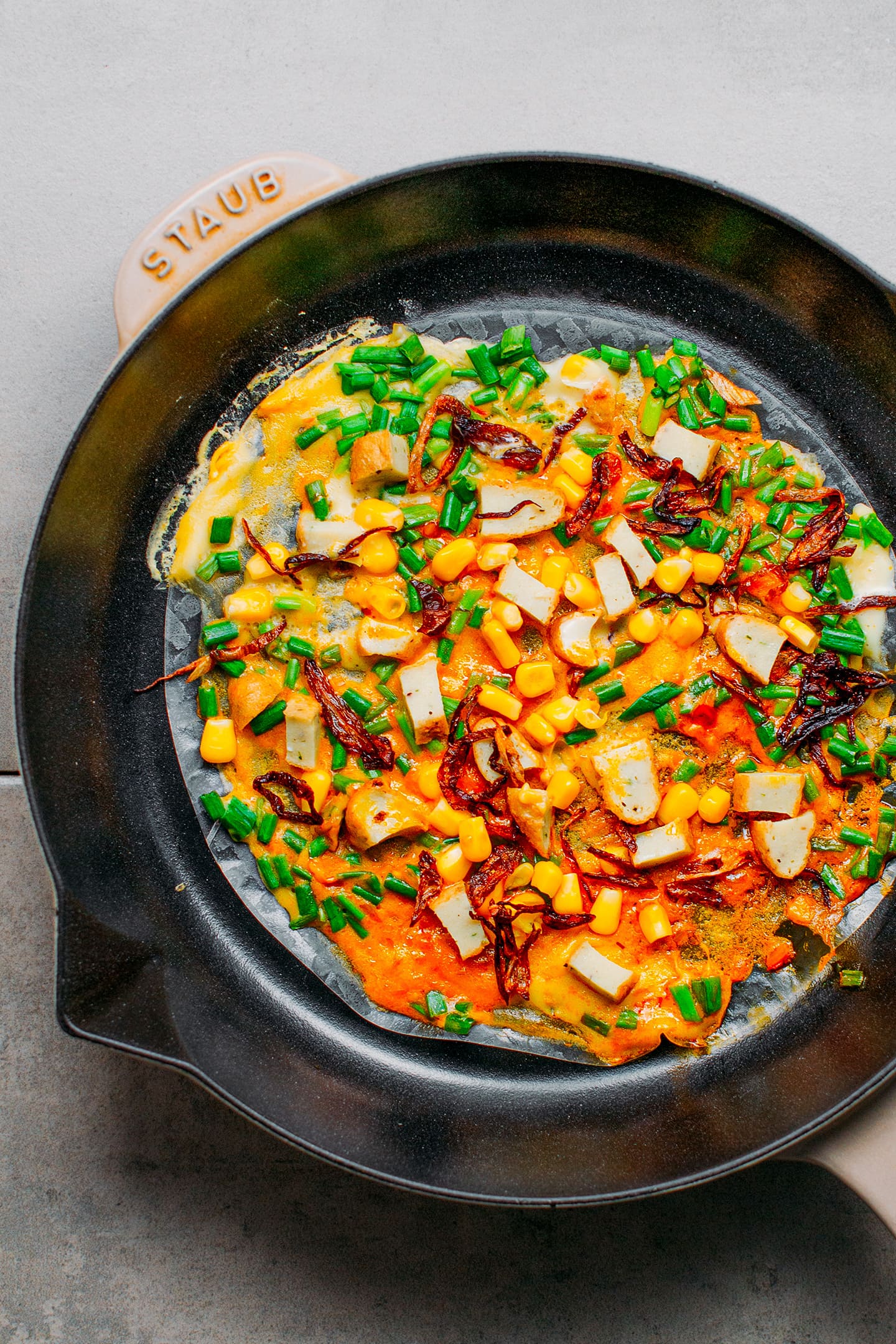 Vegan Bánh Tráng Nướng topped with corn, vegan sausages, and fried shallots in a skillet.