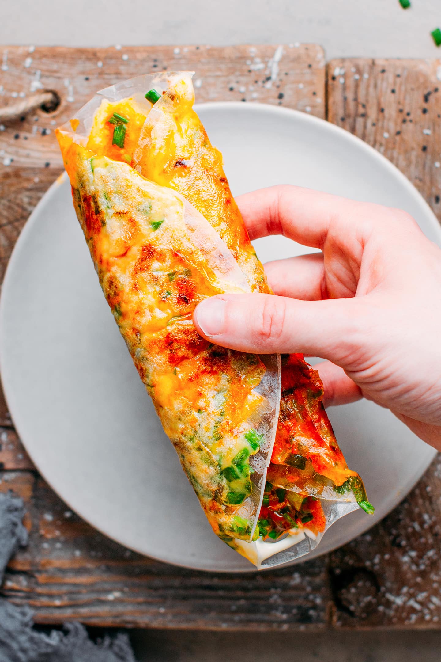 Holding a folded grilled rice paper sheet filled with sausages, vegan egg, and green onions.