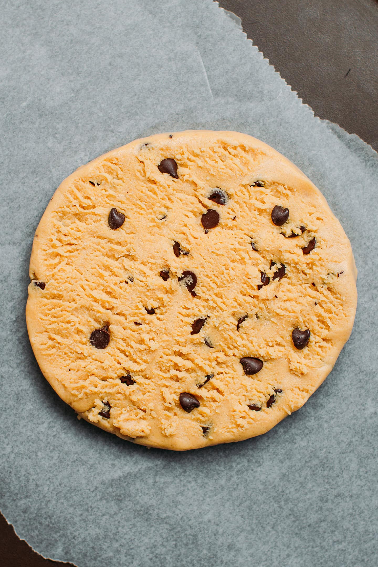 Unbaked cookie with chocolate chips on a baking sheet.