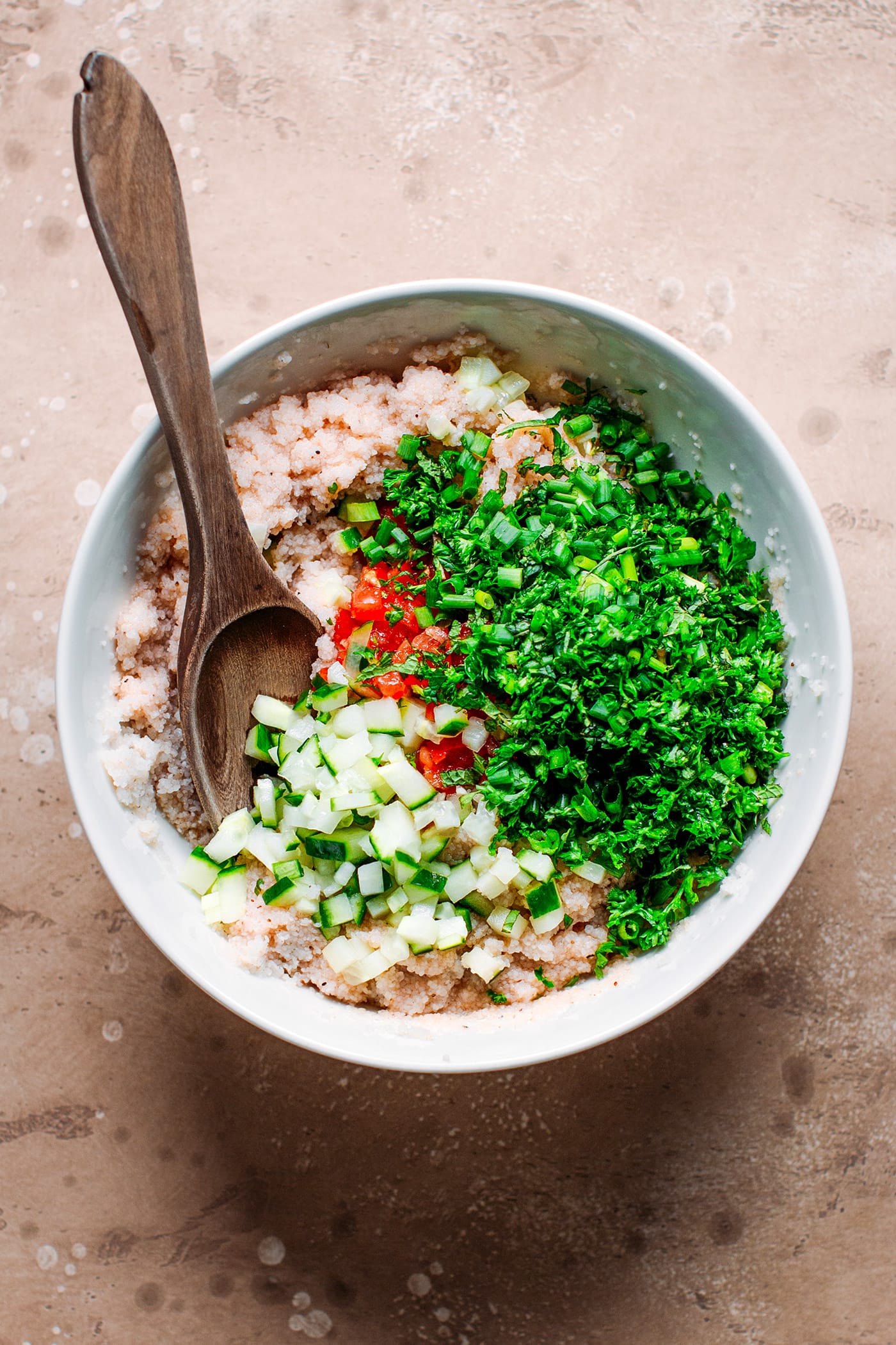 Fonio, cucumber, tomatoes, and fresh herbs in a bowl.