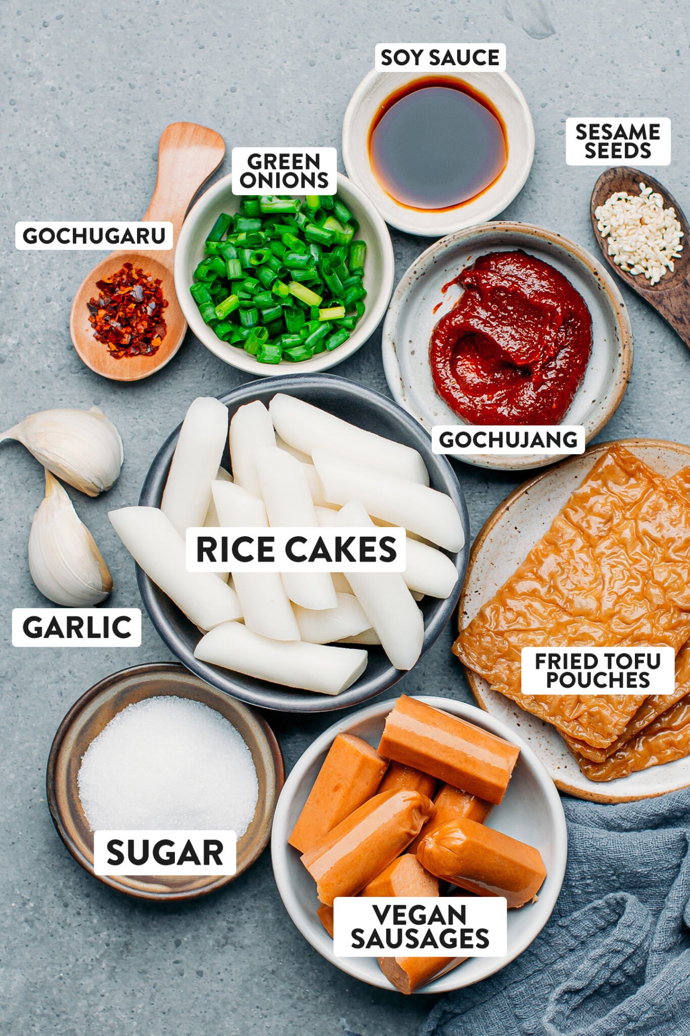 Ingredients like rice cakes, tofu, green onions, gochujang, and vegan sausages.