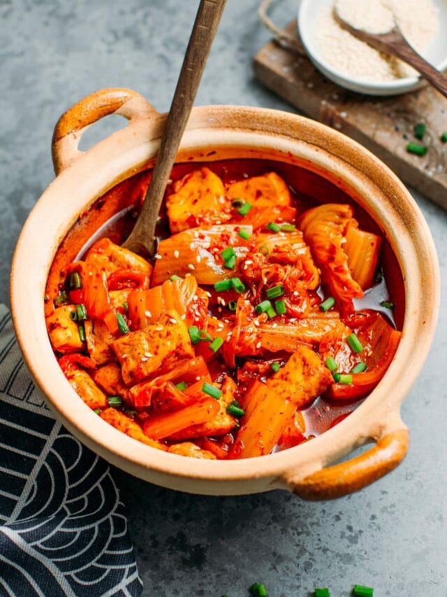 Kimchi stew in a clay pot, with tofu and green onions.