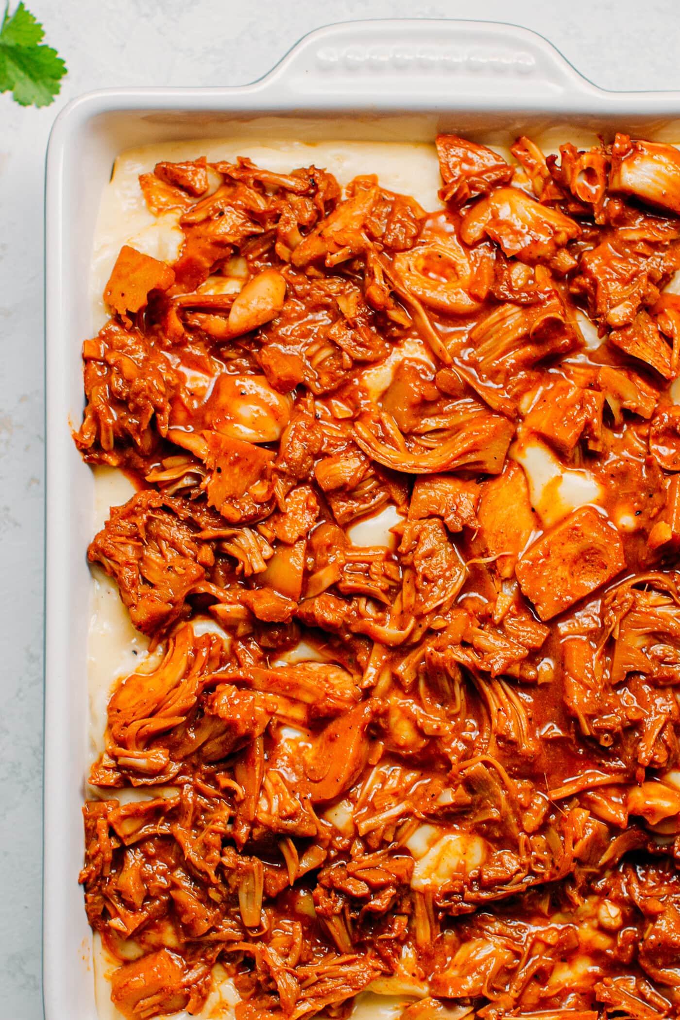 BBQ jackfruit on top of bechamel sauce, in a baking dish.