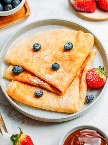 Vegan French crêpes with powdered sugar, blueberries, and strawberries.