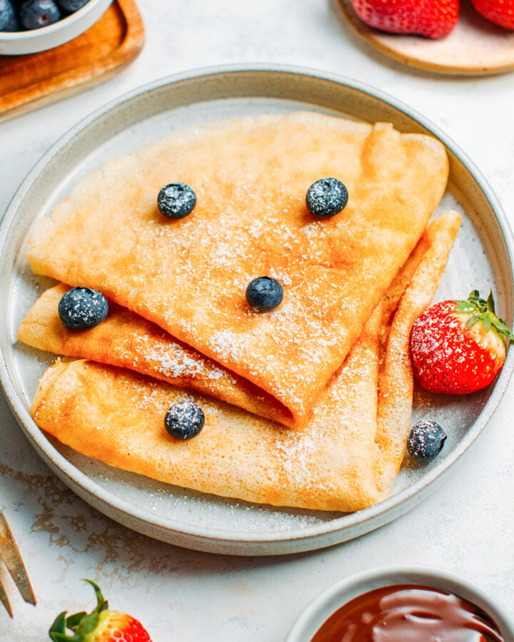 Vegan French crêpes with powdered sugar, blueberries, and strawberries.