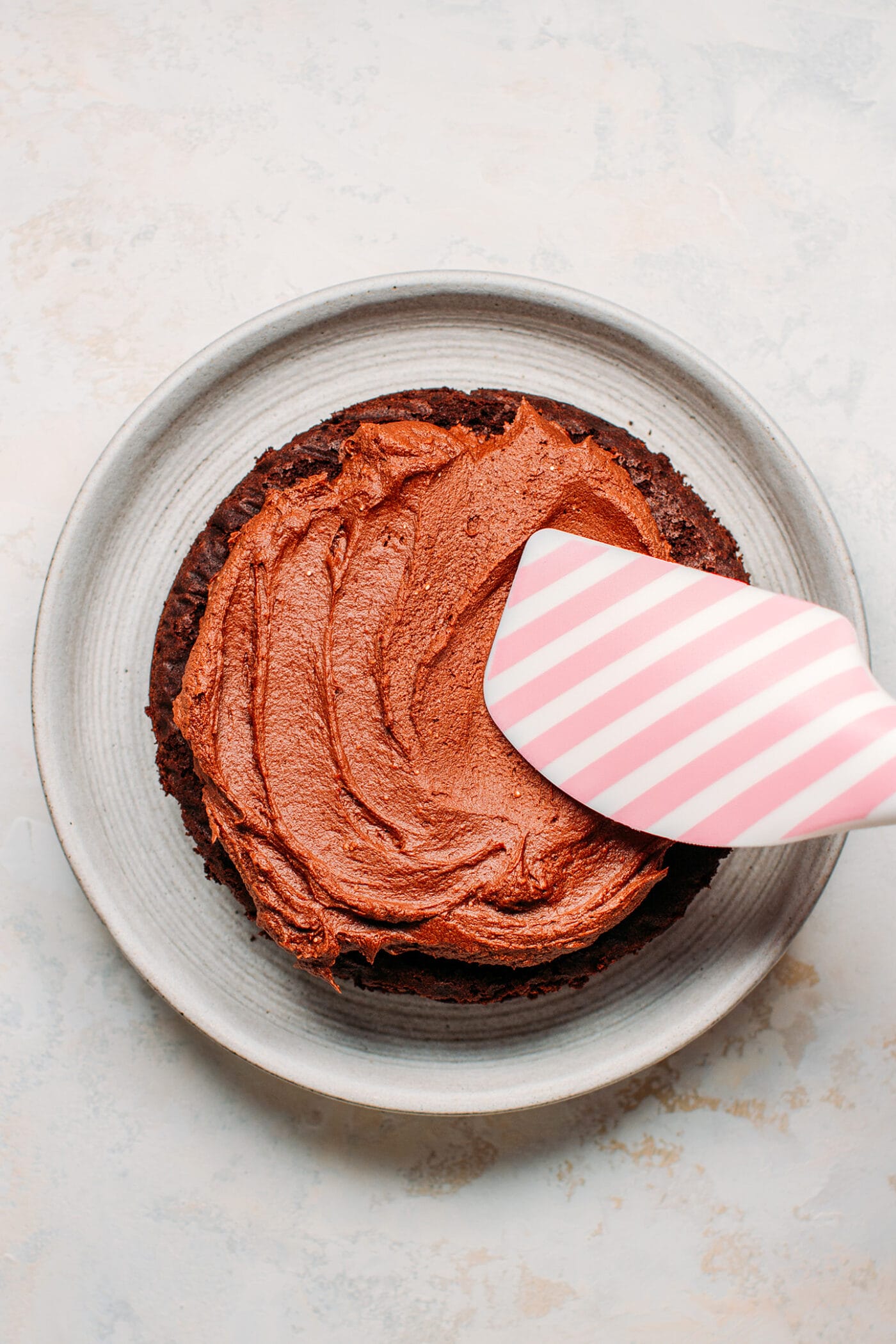 Frosting the top of a chocolate layer cake.