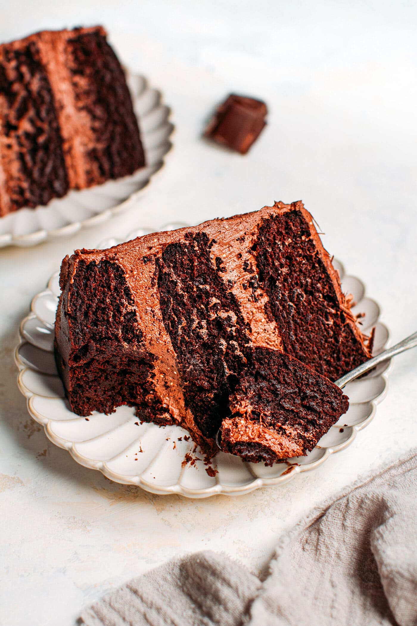 Piece of vegan chocolate layer cake with frosting on a plate.