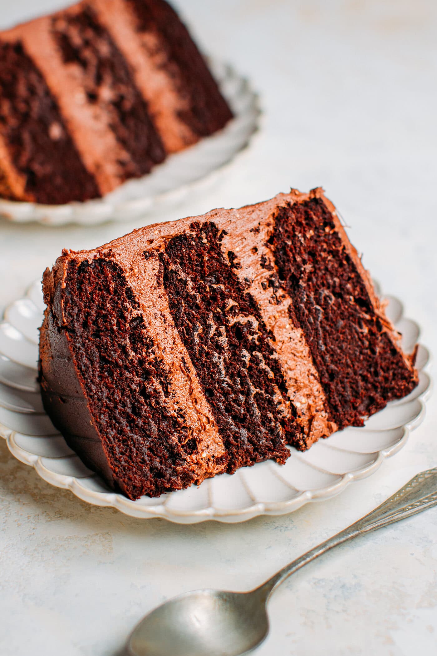 Slice of vegan chocolate layer cake with frosting on a plate.