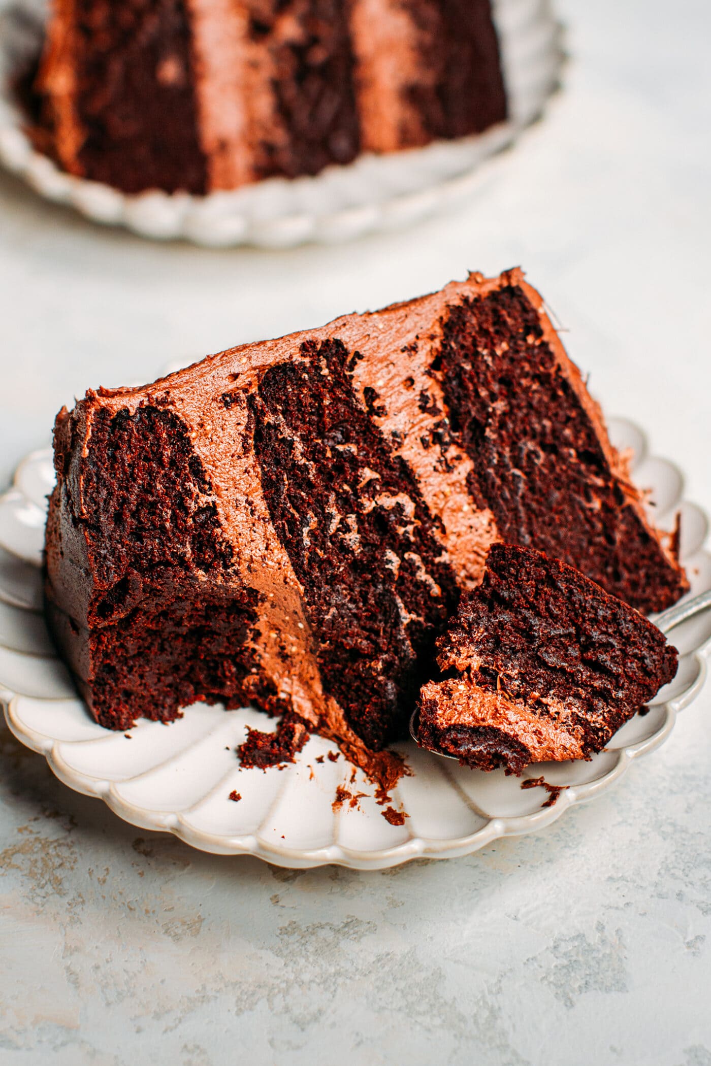 Slice of vegan chocolate layer cake with frosting on a plate.