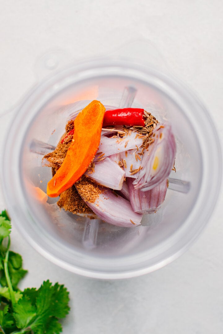 Shallots, turmeric, chili, and cumin seeds in a blender.