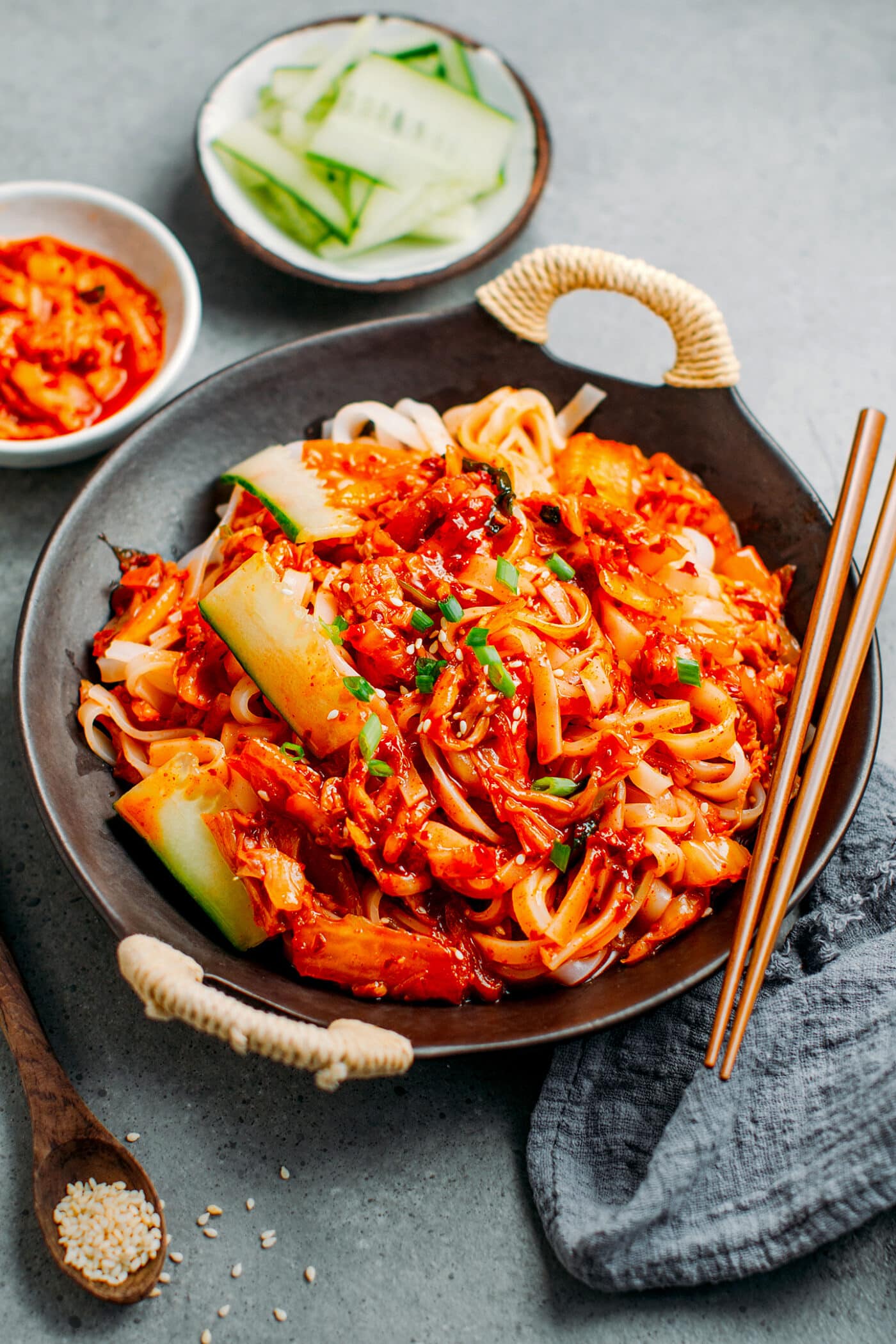 Kimchi noodles topped with sesame seeds, cucumber, and scallions.