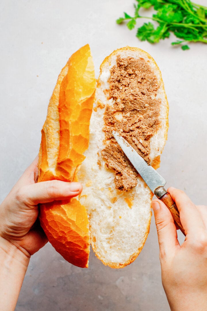 Spreading vegan paté on a banh mi sandwich.