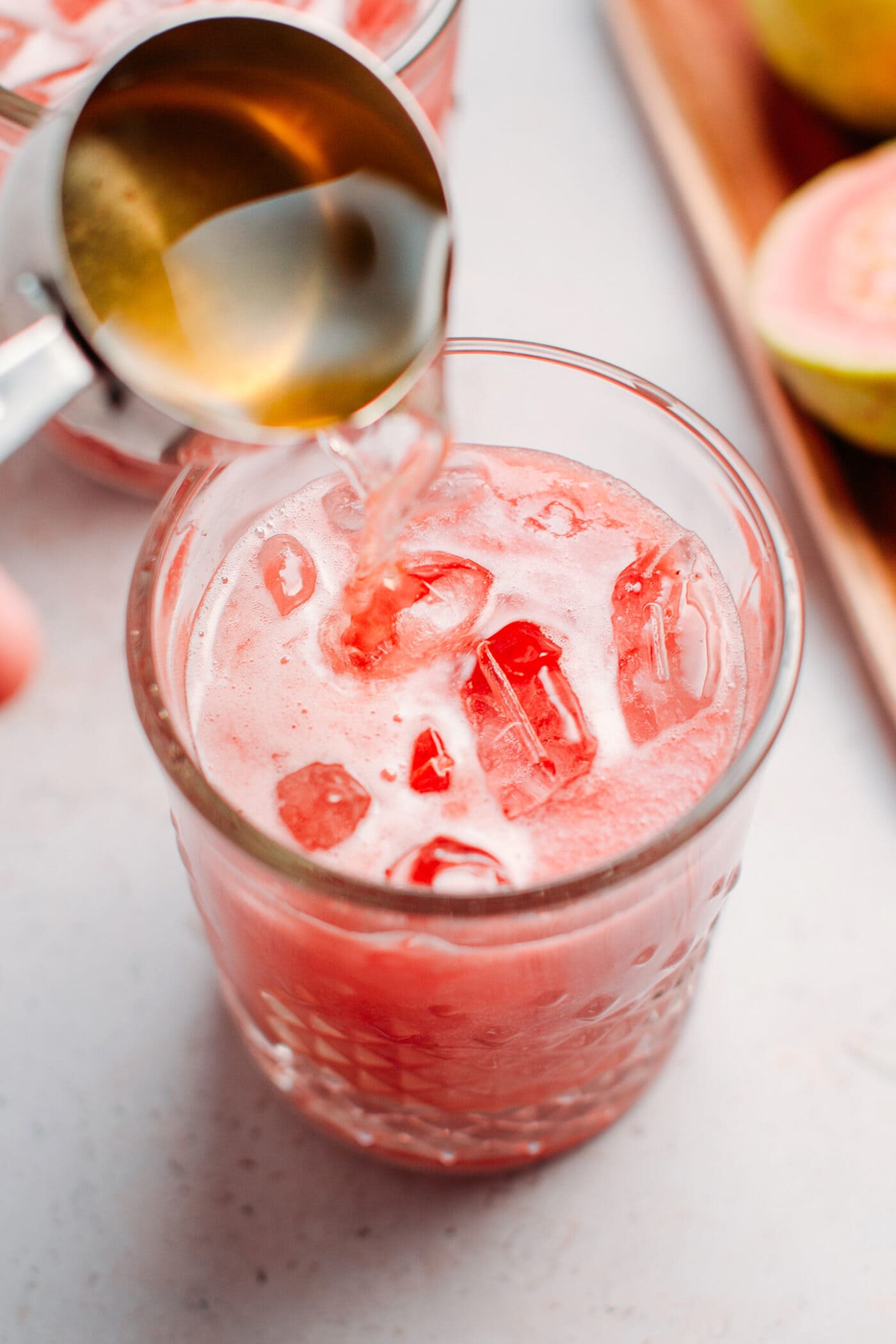 Pouring jasmine tea over guava juice in a glass.