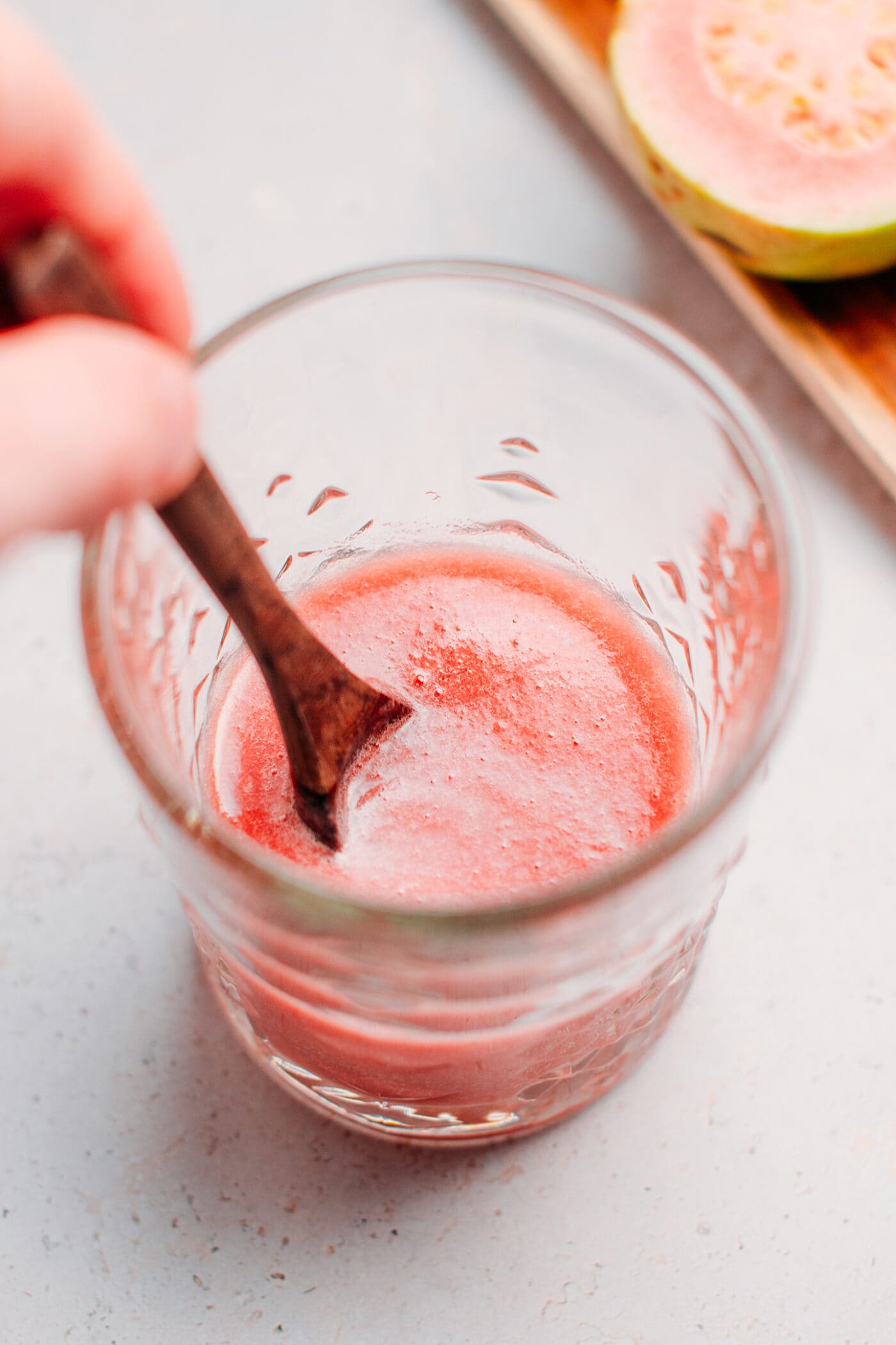 Stirring maple syrup with guava juice in a glass.