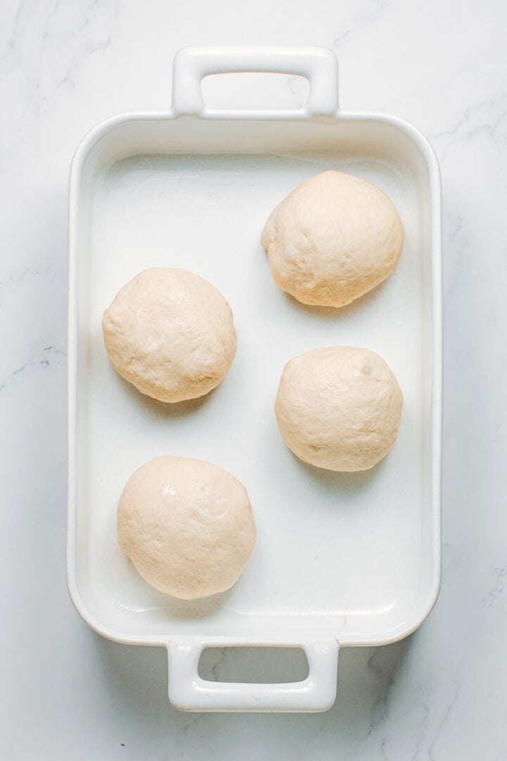 Balls of pizza dough in a baking dish.