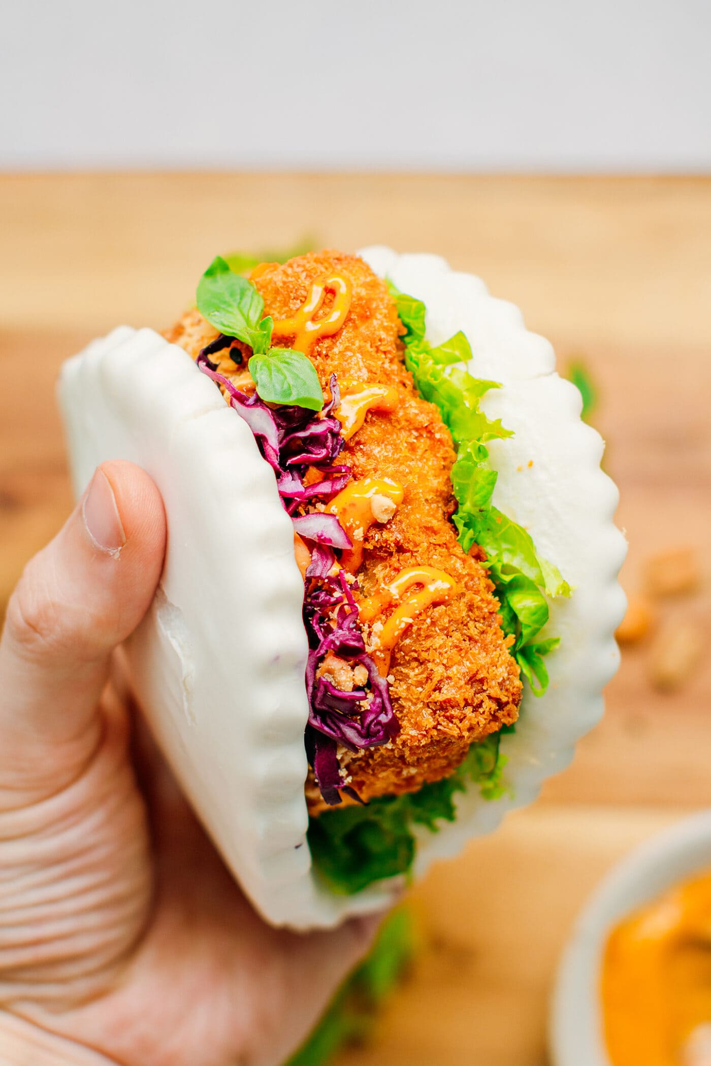 Holding gua bao with katsu tempeh, peanuts, red cabbage, and lettuce.