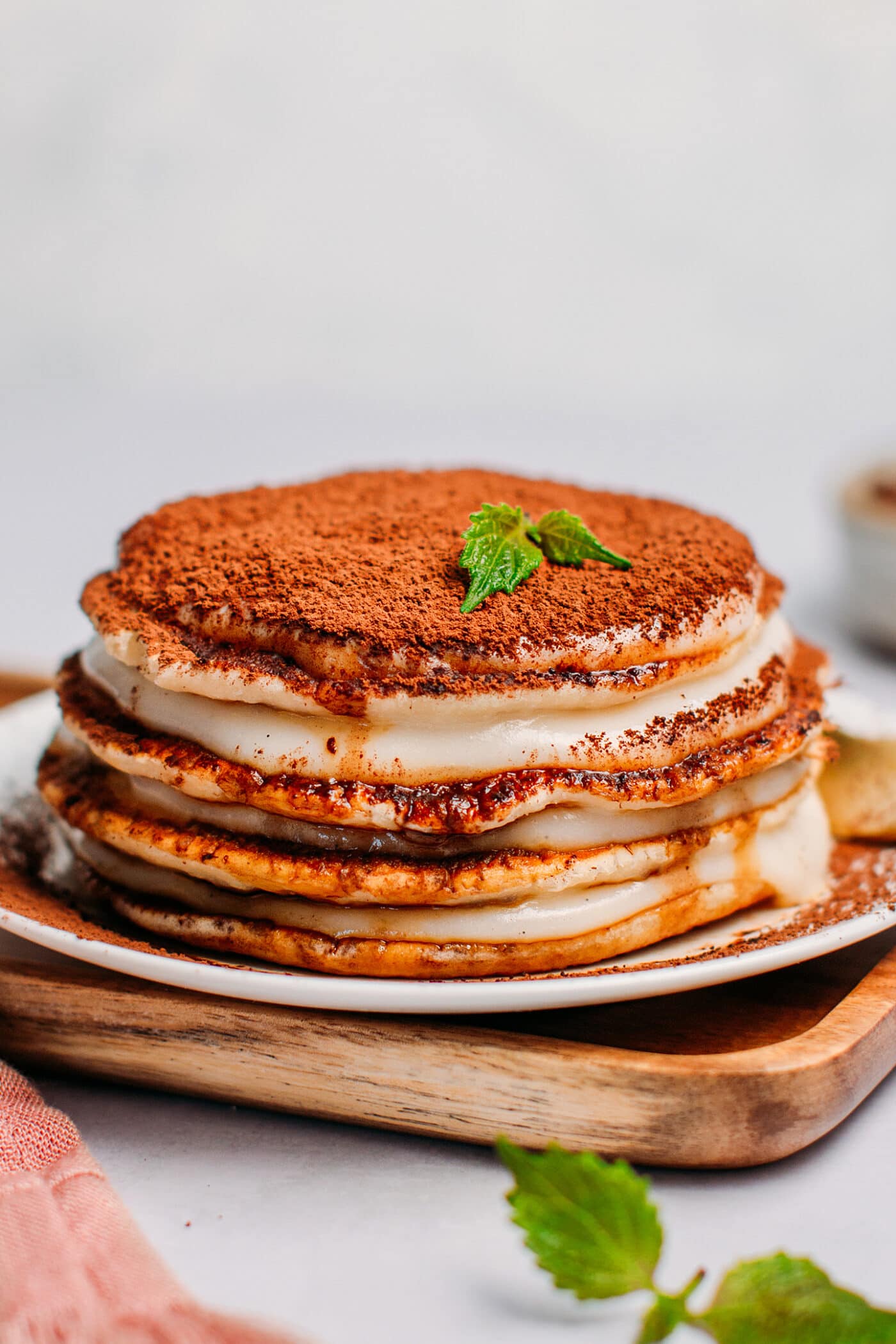 Vegan tiramisu pancakes sprinkled with cacao powder and topped with mint leaves.