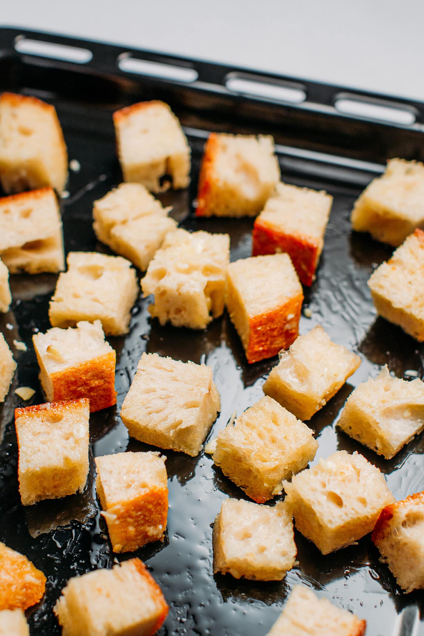 Diced bread coated with oil on a baking sheet.