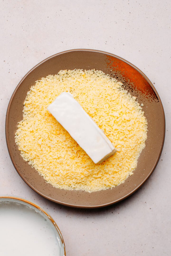 Stick of tofu on a plate of panko breadcrumbs.