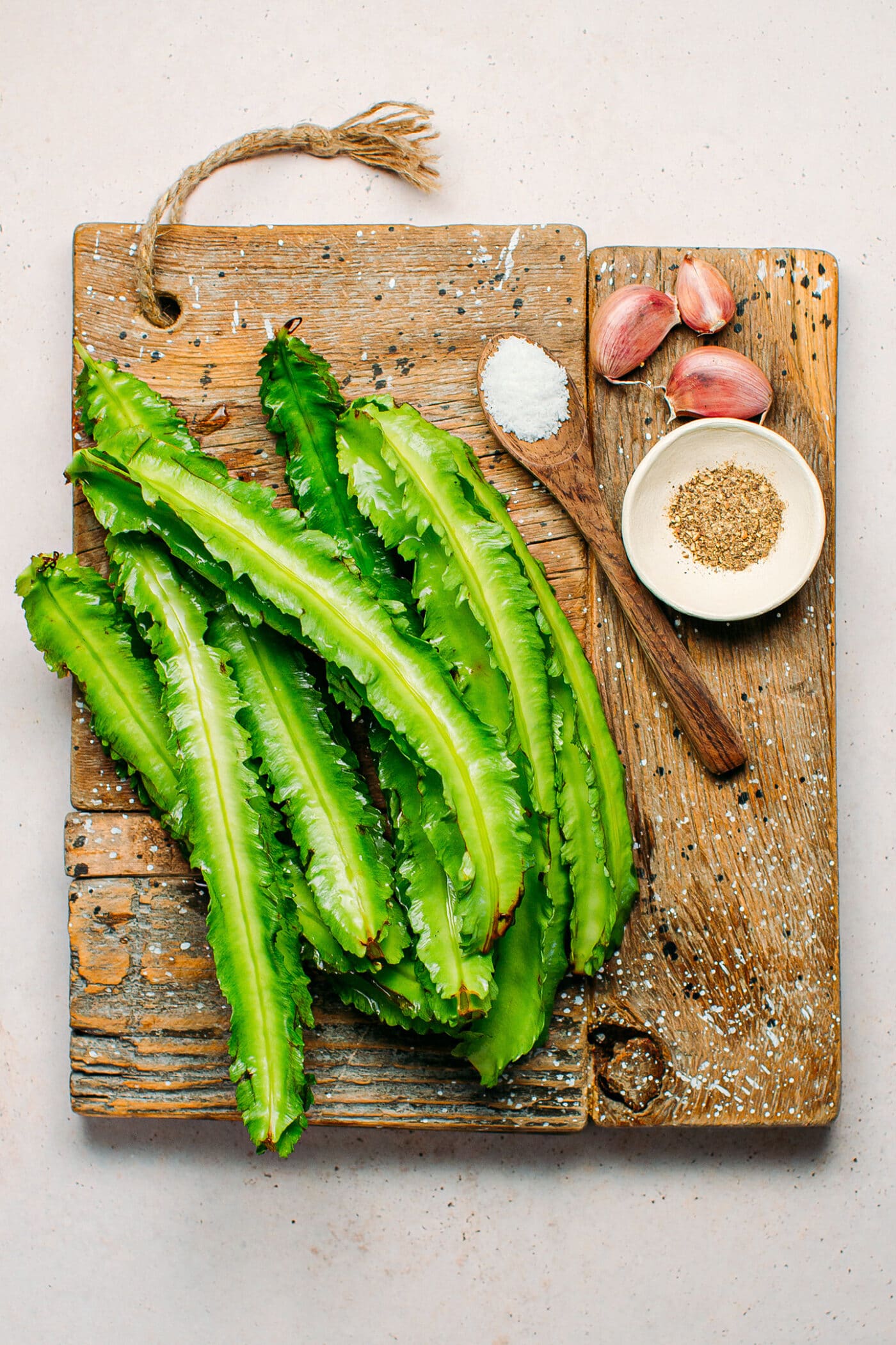 Ingredients like winged beans, garlic, salt, and pepper on a cutting board.