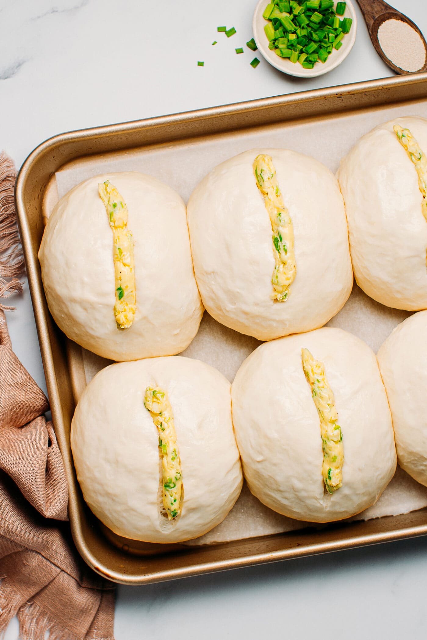 Dinner rolls filled with garlic butter on a baking sheet.