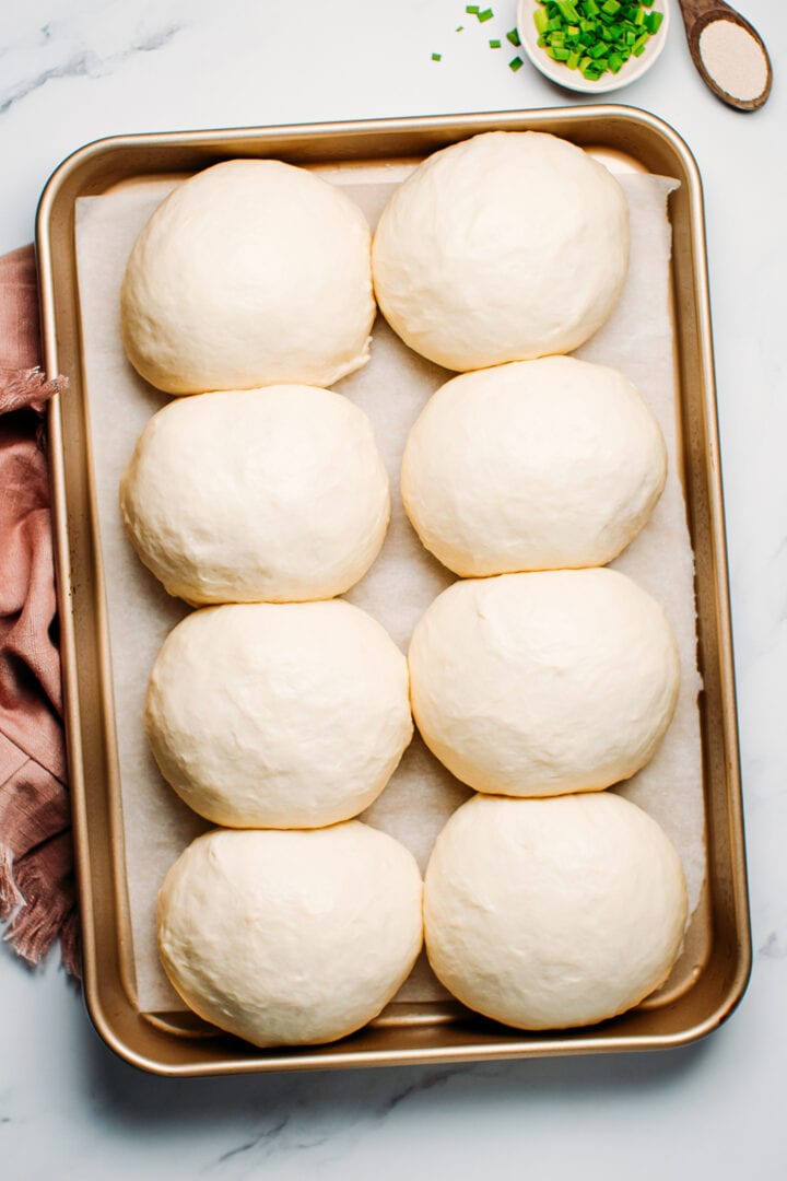 Balls of dough after a second rise on a baking sheet.