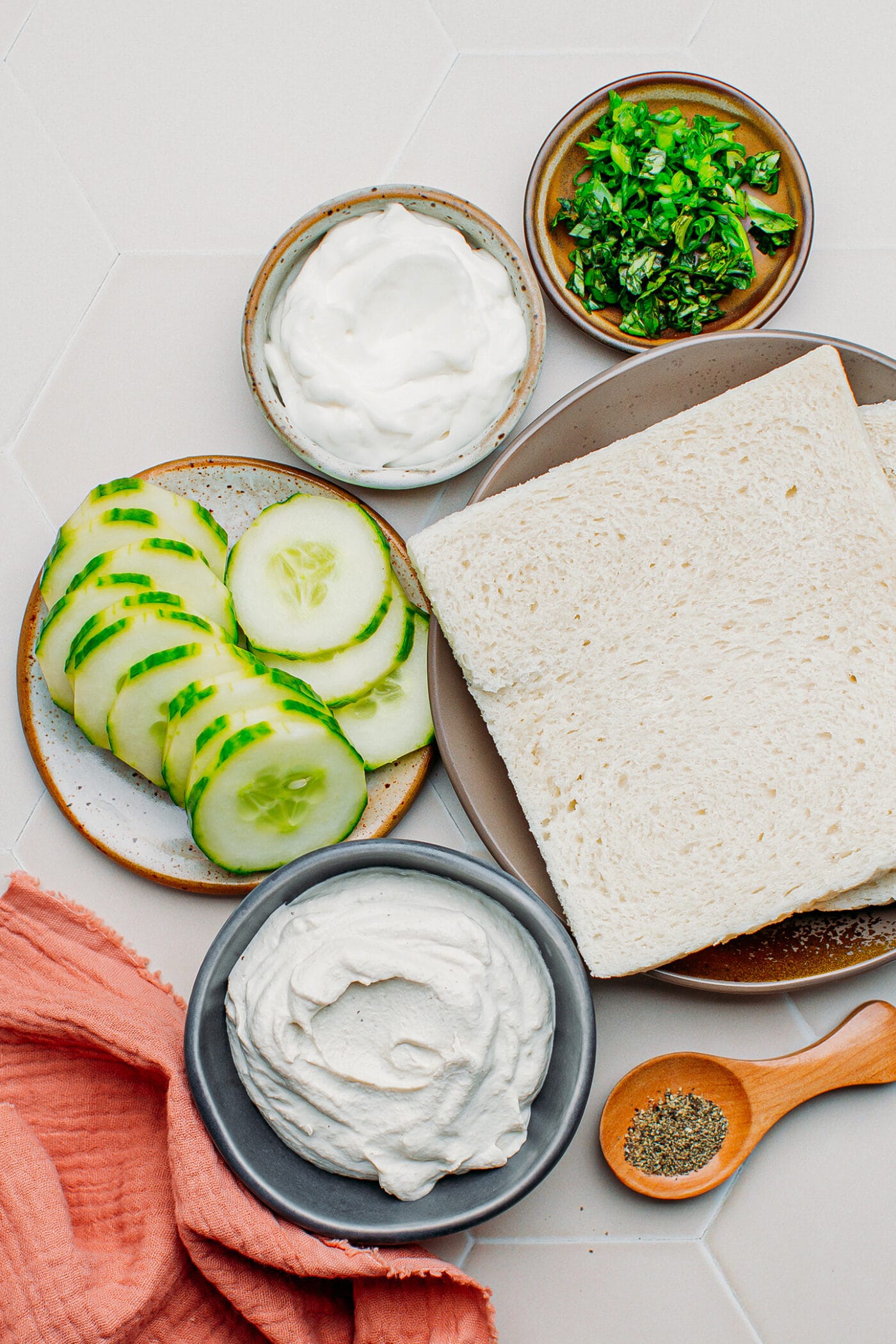 Ingredients like cucumbers, sandwich bread, vegan cream cheese, and mayo.