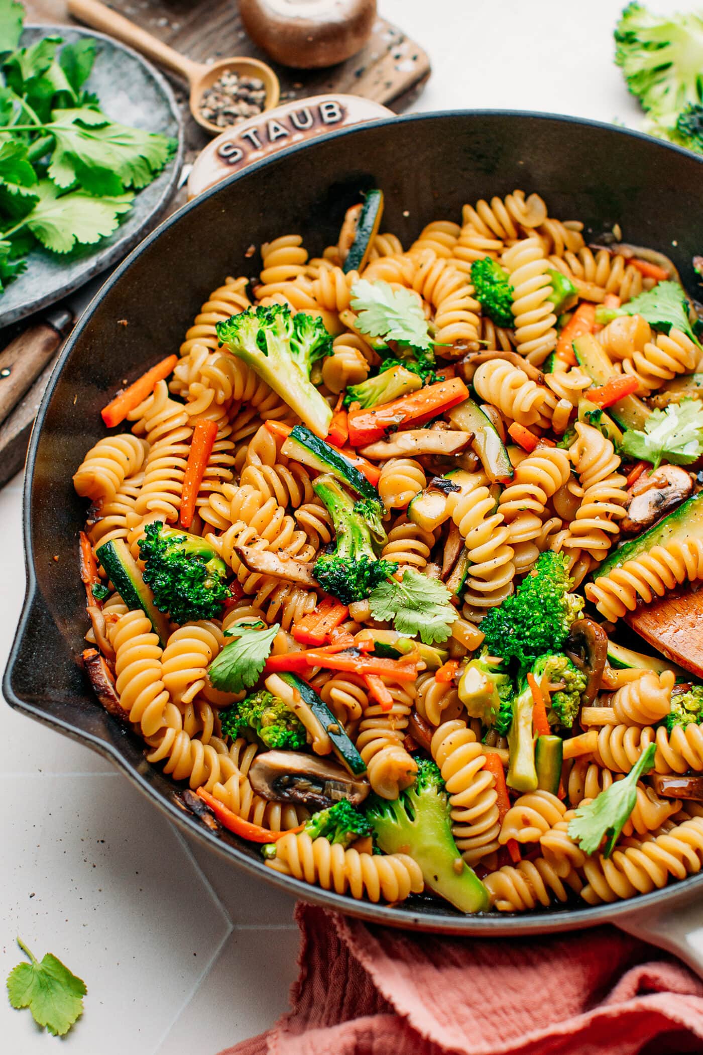 Pasta stir-fry with broccoli, carrots, and mushrooms in a skillet.