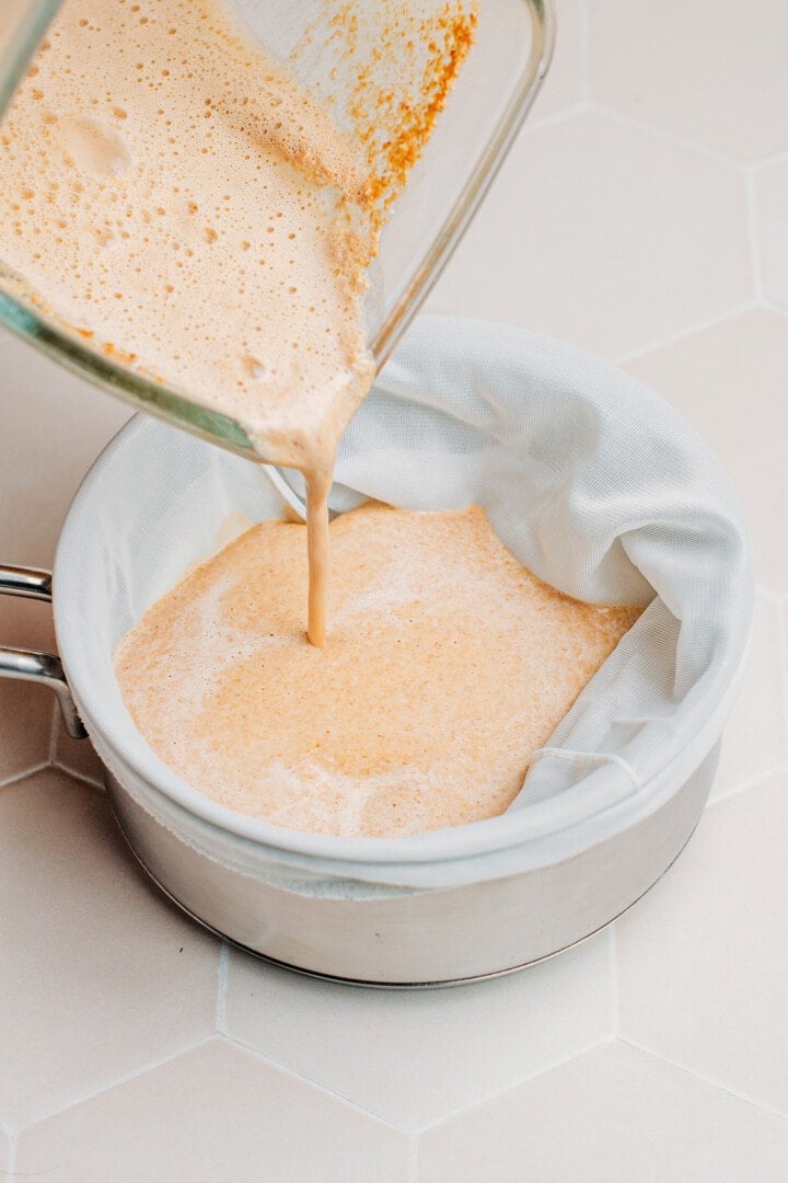 Pouring milk into a saucepan covered with a nut milk bag.