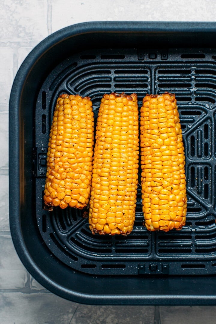 Roasted ear of corn in the basket of an air fryer.