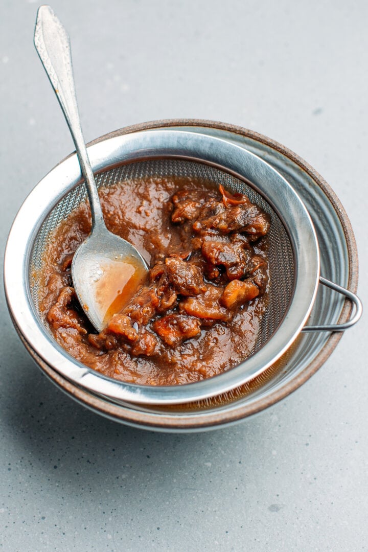 Straining tamarind pulp over a bowl.