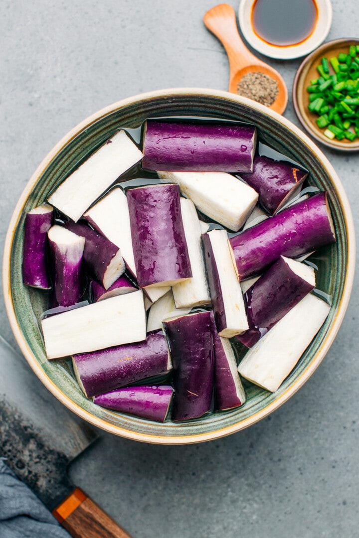 Sliced eggplant soaking in a bowl of water.