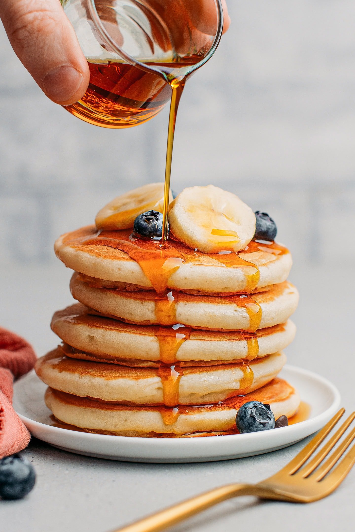 Stack of vegan pancakes drizzled with maple syrup and topped with banana slices and blueberries.