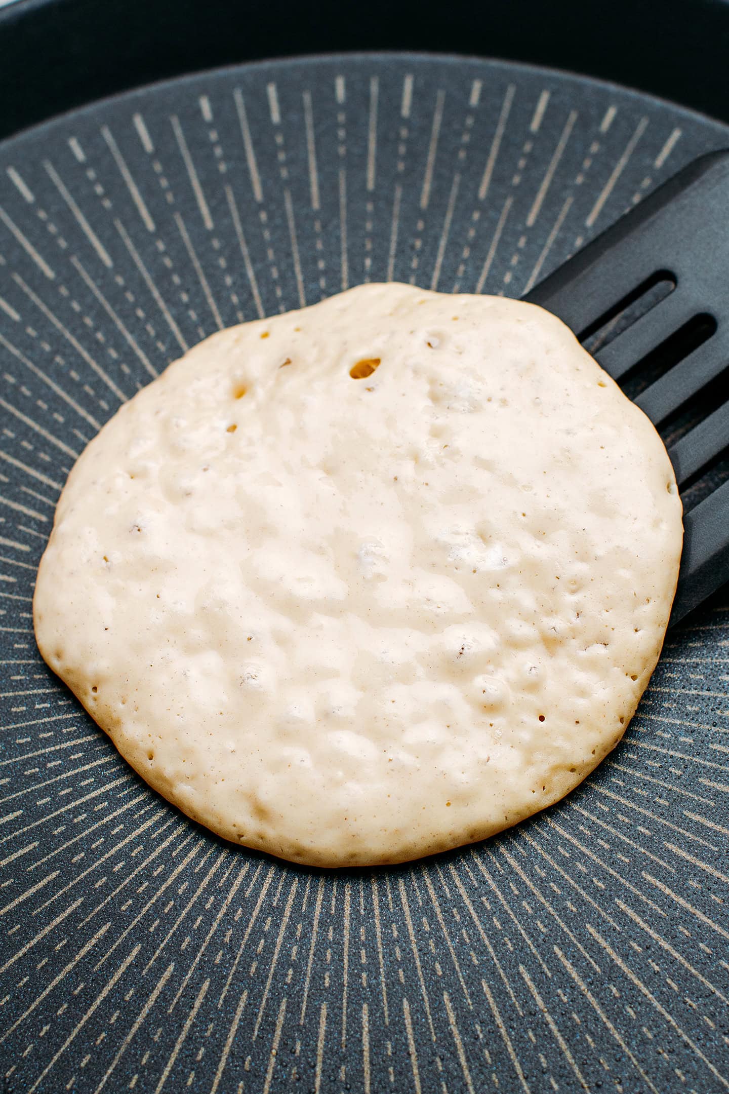 Flipping a pancakes on a non-stick pan using a spatula.