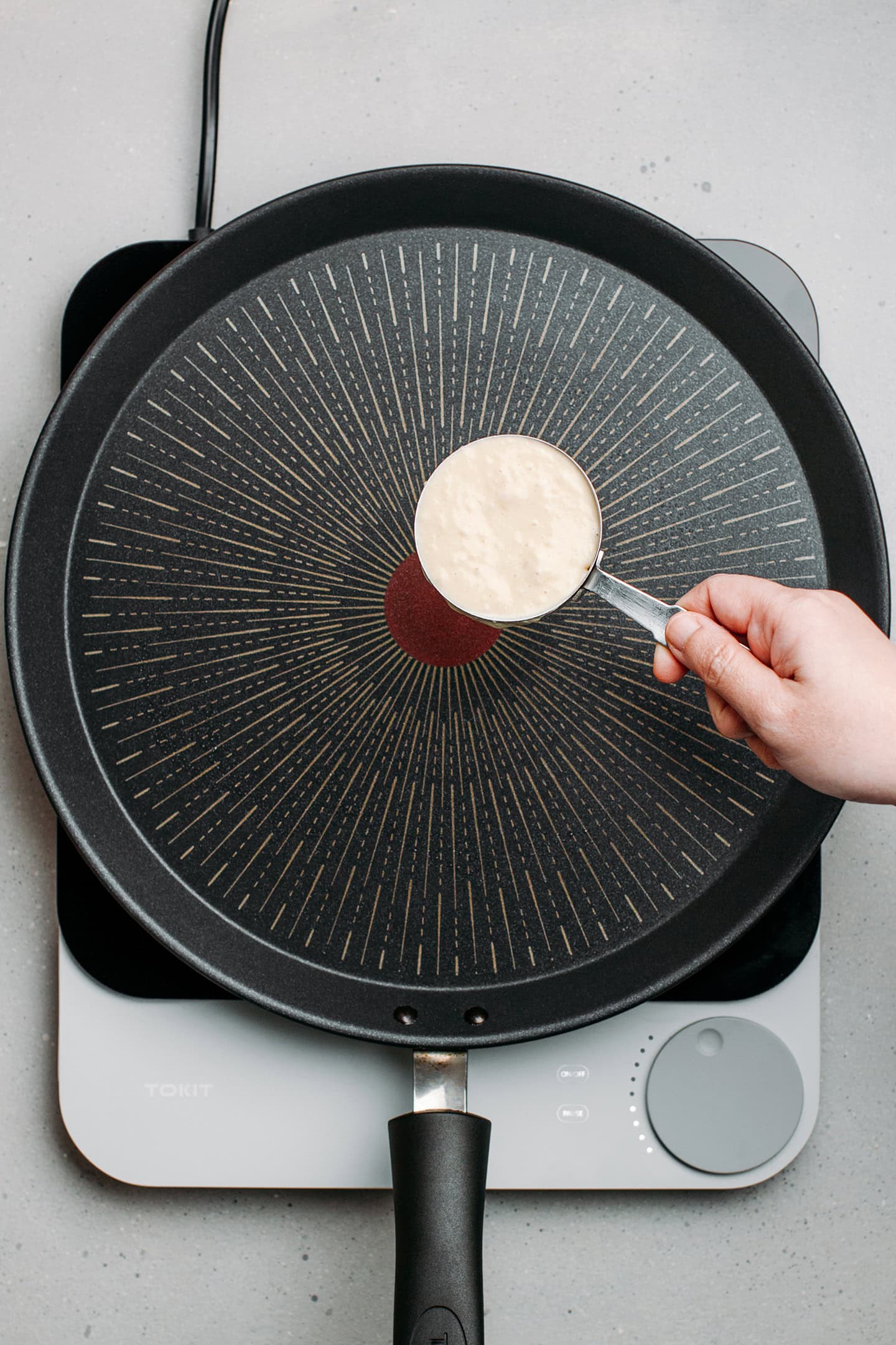 Holding 1/3 cup of pancake batter over a non-stick skillet.
