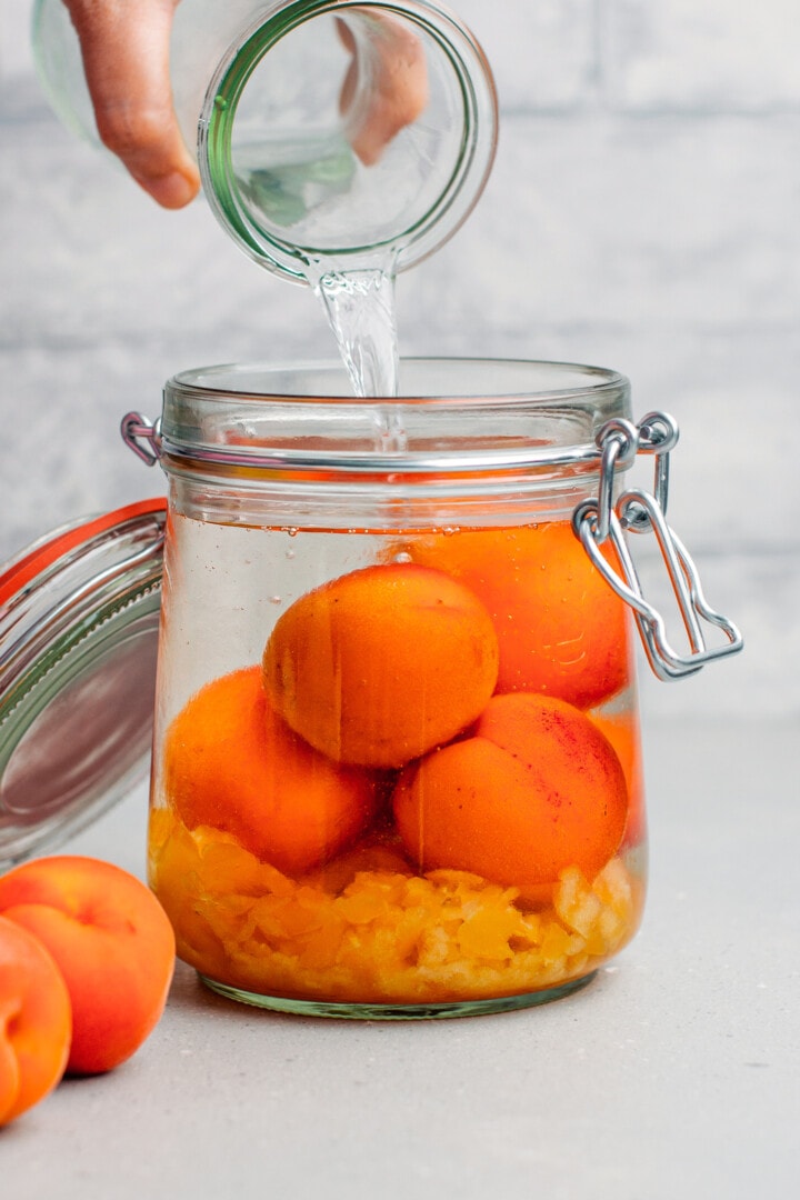 Pouring vodka over apricots, in a jar.