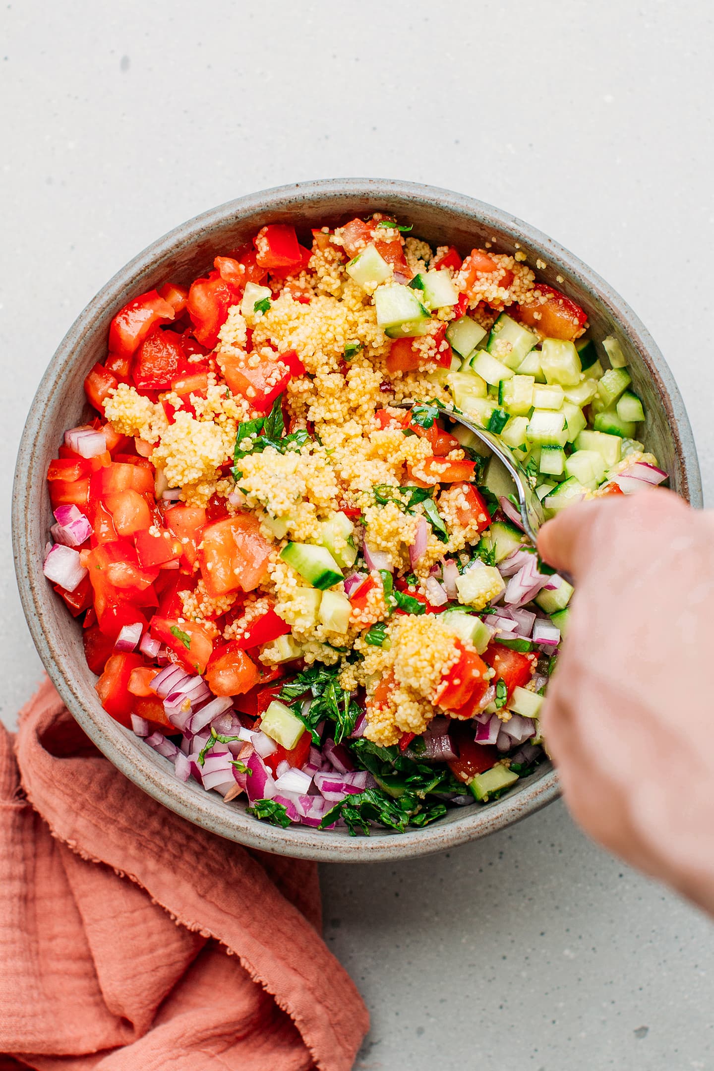 Couscous salad with cucumbers, tomatoes, red onions, and fresh herbs in a bowl.