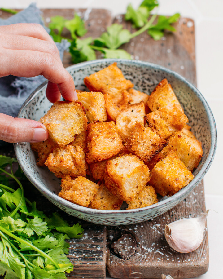 Hand holding a piece of crouton over a serving bowl.