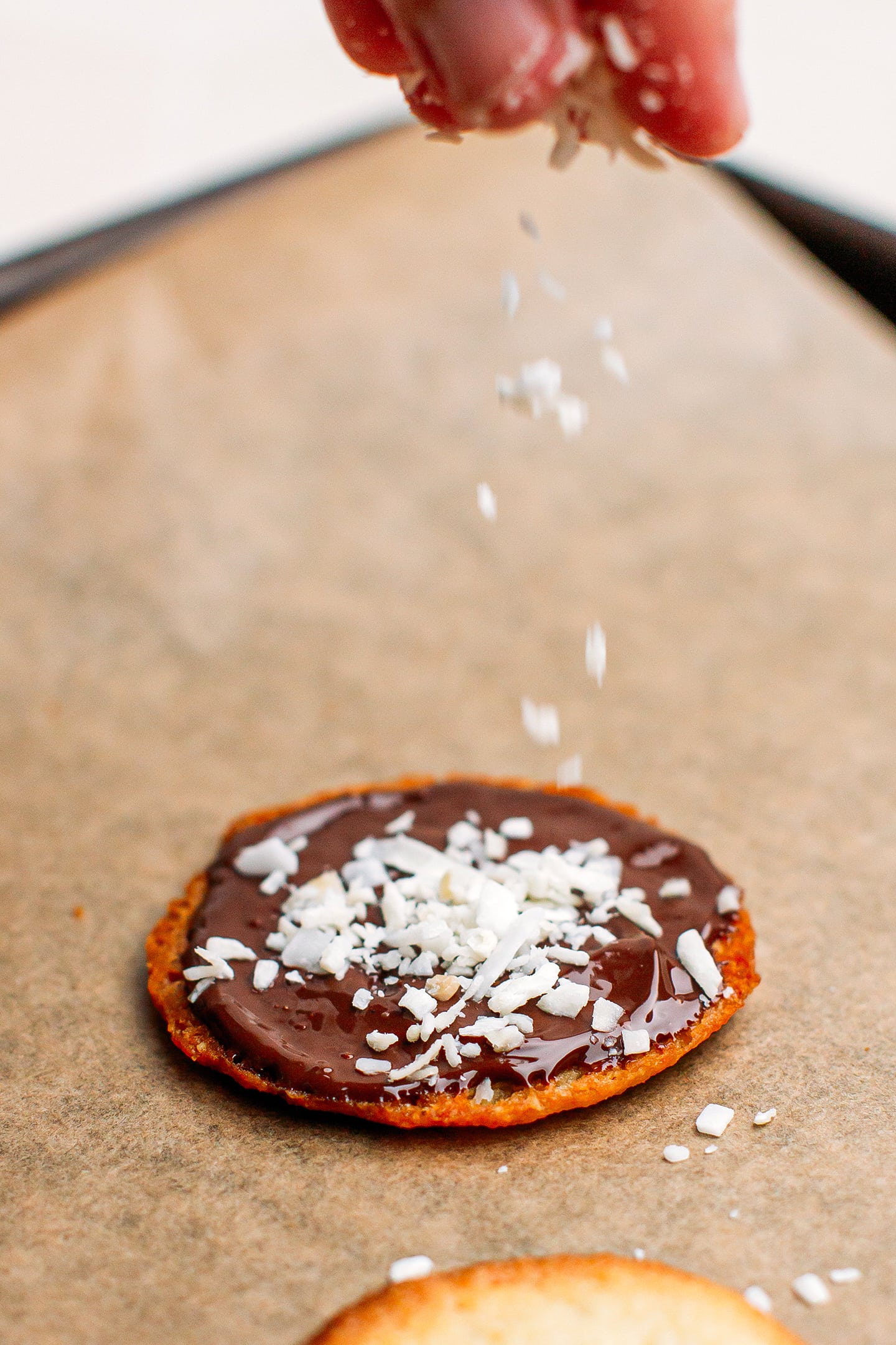 Sprinkling shredded coconut over dark chocolate cookies.